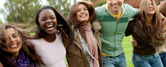 Group of friends laughing with each other outside. There are four girls and one boy and there is a red bridge behind them.