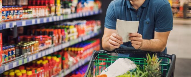 Guy with a shopping list and cart in a grocery store aisle.