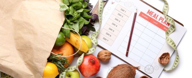 There is a brown paper bag with health foods spilling out. On the other side is a clip board and pen with a paper that has a meal plan sheet on it.