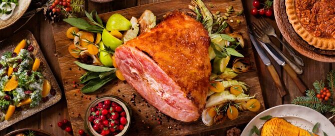 There is a feast on a wooden table that includes ham and carrots.